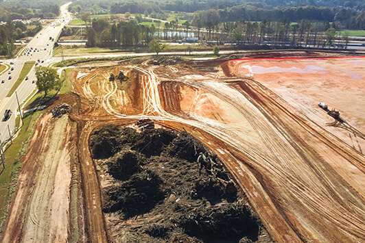 Aerial view of a large construction site with earthmoving equipment grading soil for infrastructure development