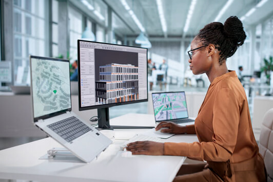 Engineer working at a desk with computer monitors displaying building models and site plans