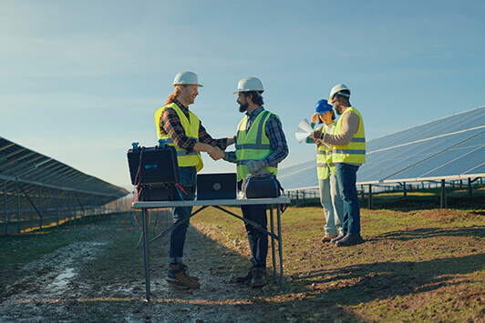 Engineers inspecting equipment and shaking hands at a solar energy installation site