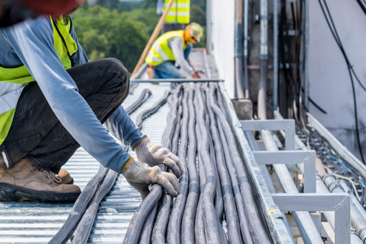 Workers installing and organizing electrical cables along a rooftop cable tray