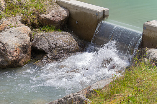 Small concrete spillway channel releasing water between rocks and vegetation